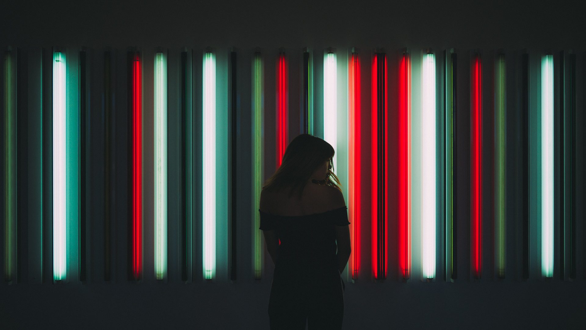 Abstract street photography of girl silhouette in front of red, white, and green striped lighting installation