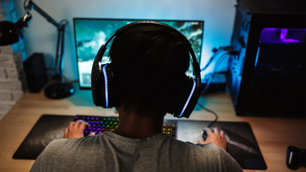 Gamer playing video games on PC with LED headphones and LED gaming keyboard