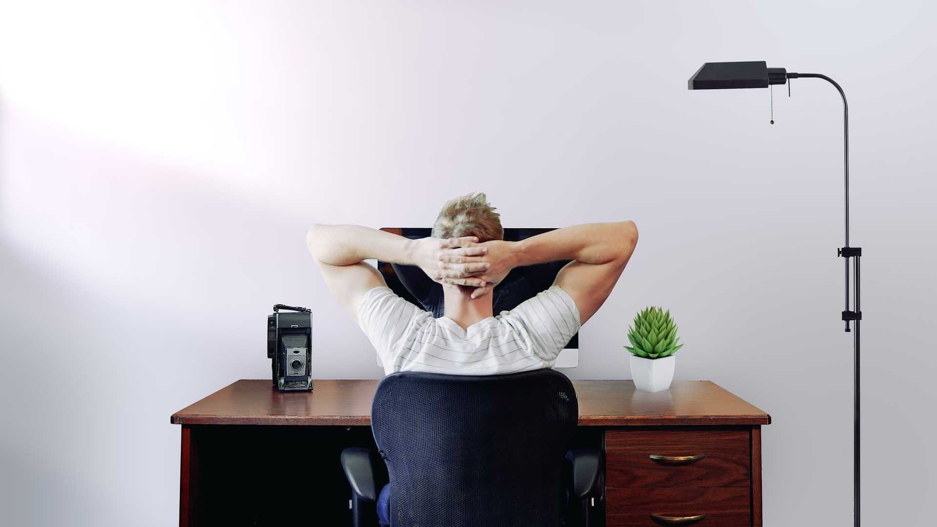 Idea development - man sitting at desk with hands behind head (thinking)
