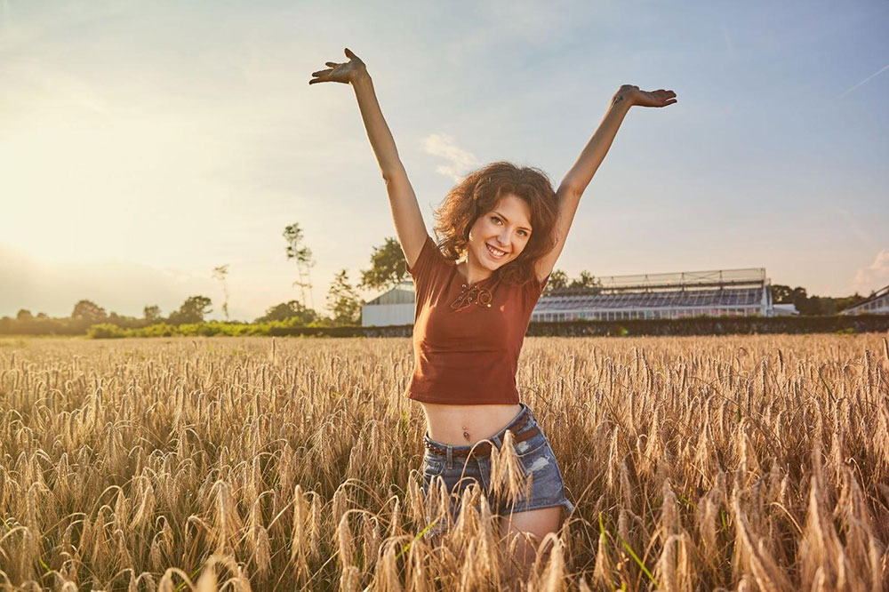 Woman poses in field of corn at sunset
